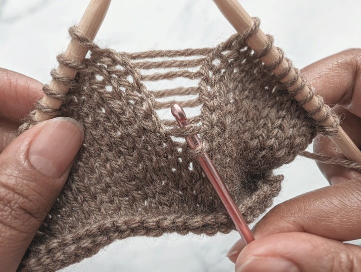 crochet hook inserted into a dropped stitch and behind the strand just above it, preparing the ladder up