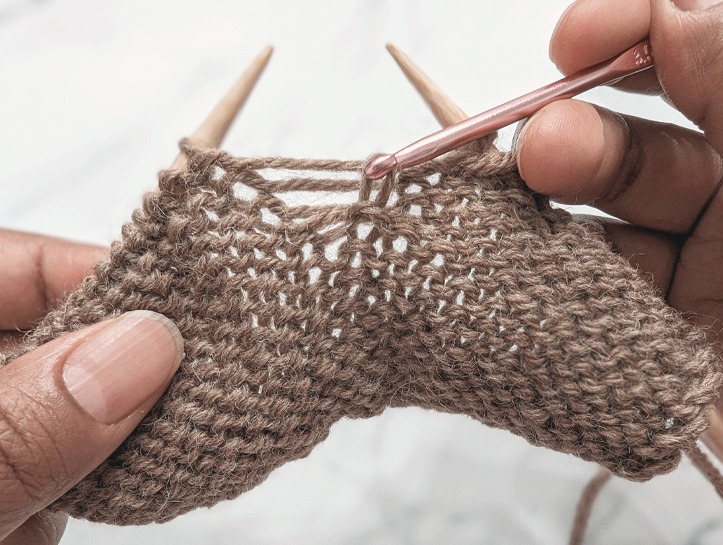 crochet hook pulling a horizontal strand through the dropped purl stitch