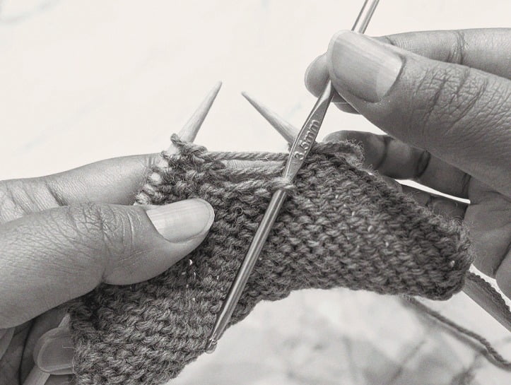 right hand pushing crochet hook down into the dropped purl stitch, preparing for the next strand