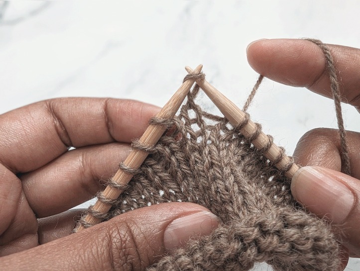 right hand knitting needle inserted into the front leg of a twisted stitch from front to back