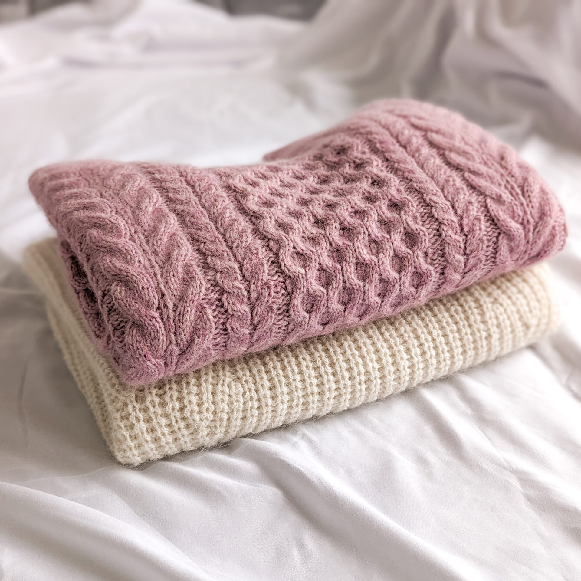 folded up white ribbed sweater underneath another folded up pink cable knit sweater